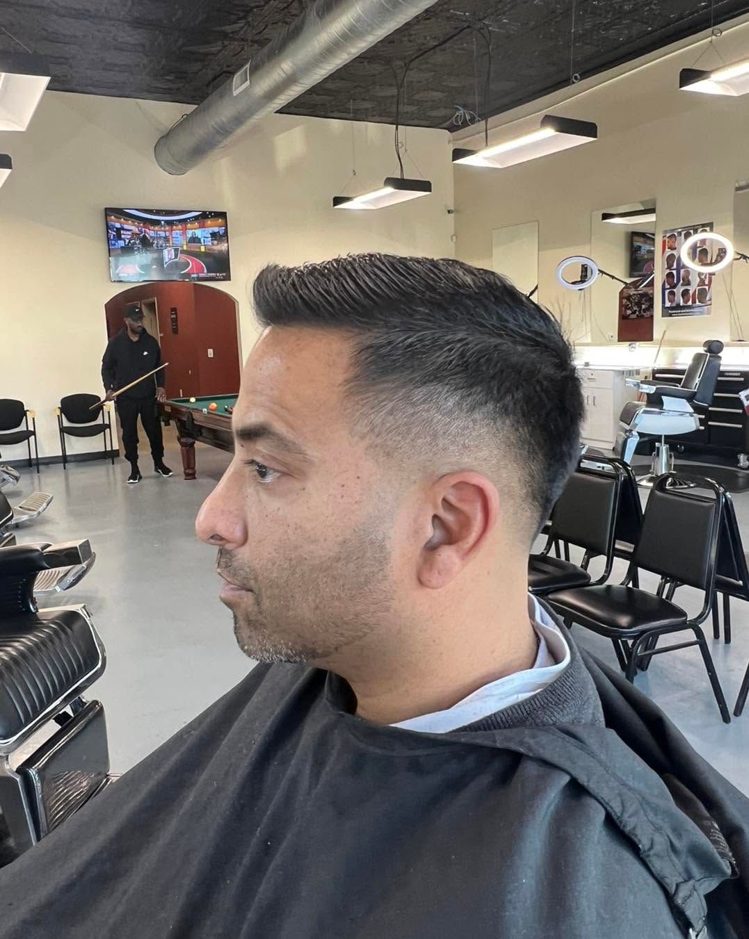 Man in a black barber cape with a fresh fade haircut seated in a barbershop salon
