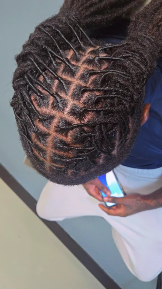 Top view of a person with neat cornrows, looking down at a phone while seated.