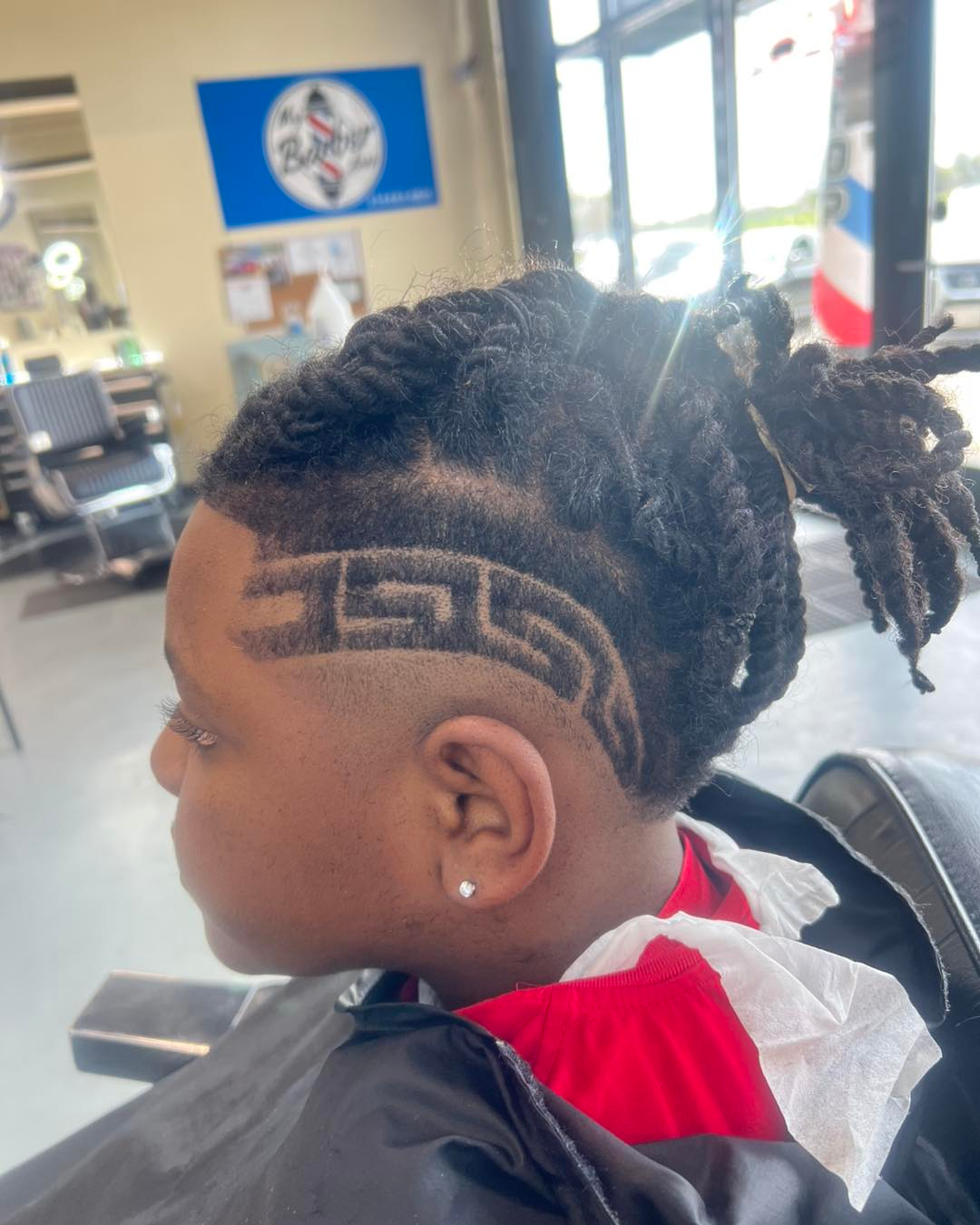 Side view of a person with a braided haircut in a barbershop, showing a shaved geometric design.