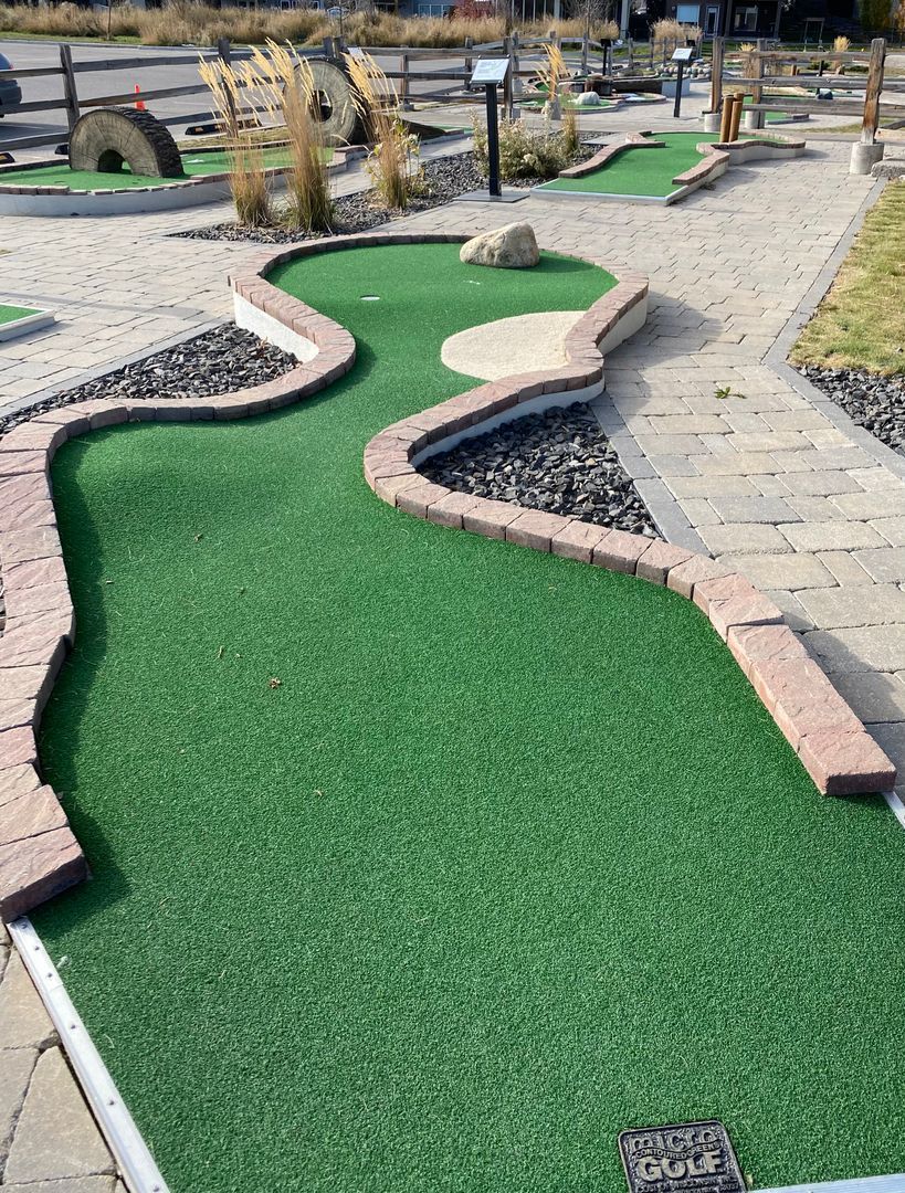 Miniature golf course green with brick borders, sand paths, and a rock feature.