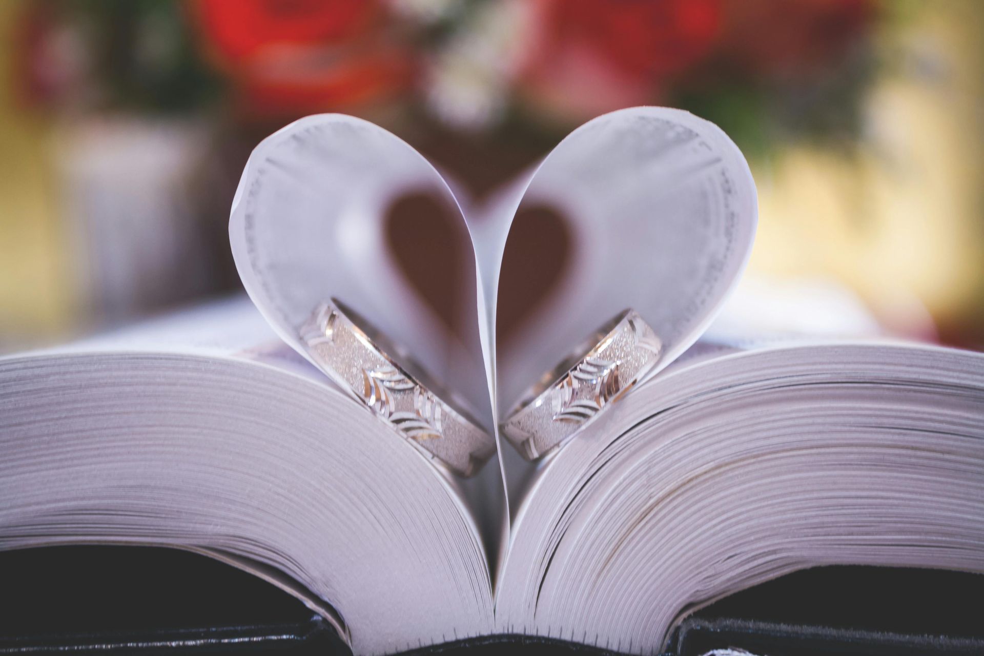 Two wedding rings are sitting on top of an open book in the shape of a heart.