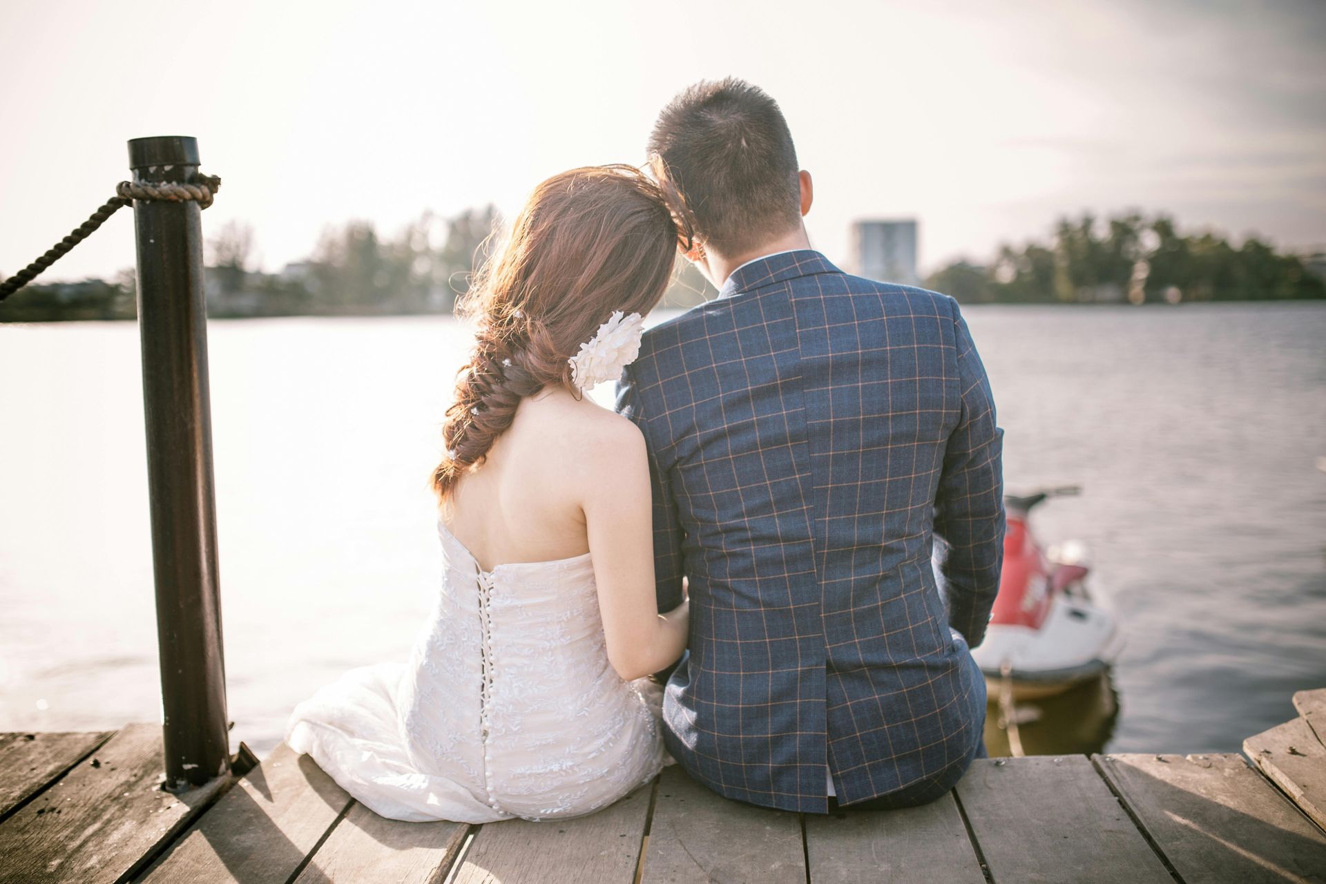 A bride and groom are sitting on a dock looking at the water.