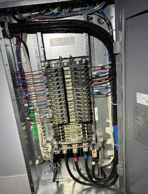 Open electrical panel with rows of breakers, wiring, and cables inside a metal cabinet
