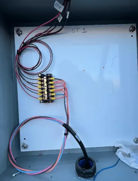 Electrical wiring panel with terminal blocks, red/black wires, and a cable entering through a blue grommet