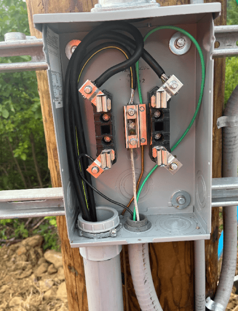 Open electrical junction box with wiring and connectors mounted on a wooden post outdoors