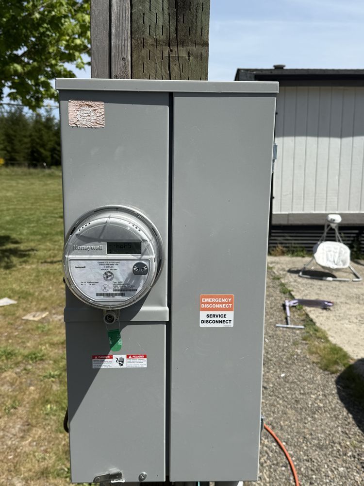Gray outdoor electrical meter cabinet beside a wooden utility pole and building wall.