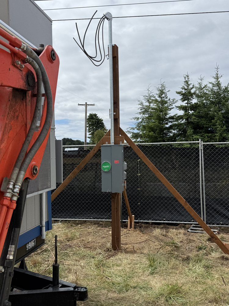 Construction equipment beside a fenced utility pole in a grassy lot under overcast sky