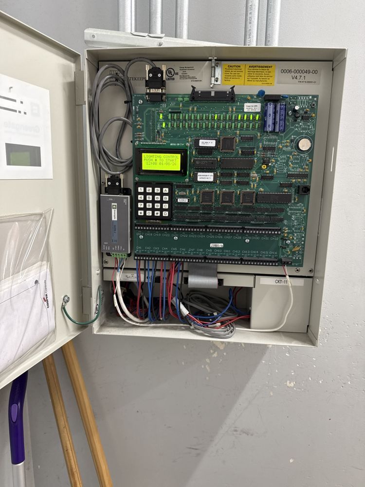 Open electrical control panel with circuit board, keypad, wiring, and hanging documents on the inside of the door