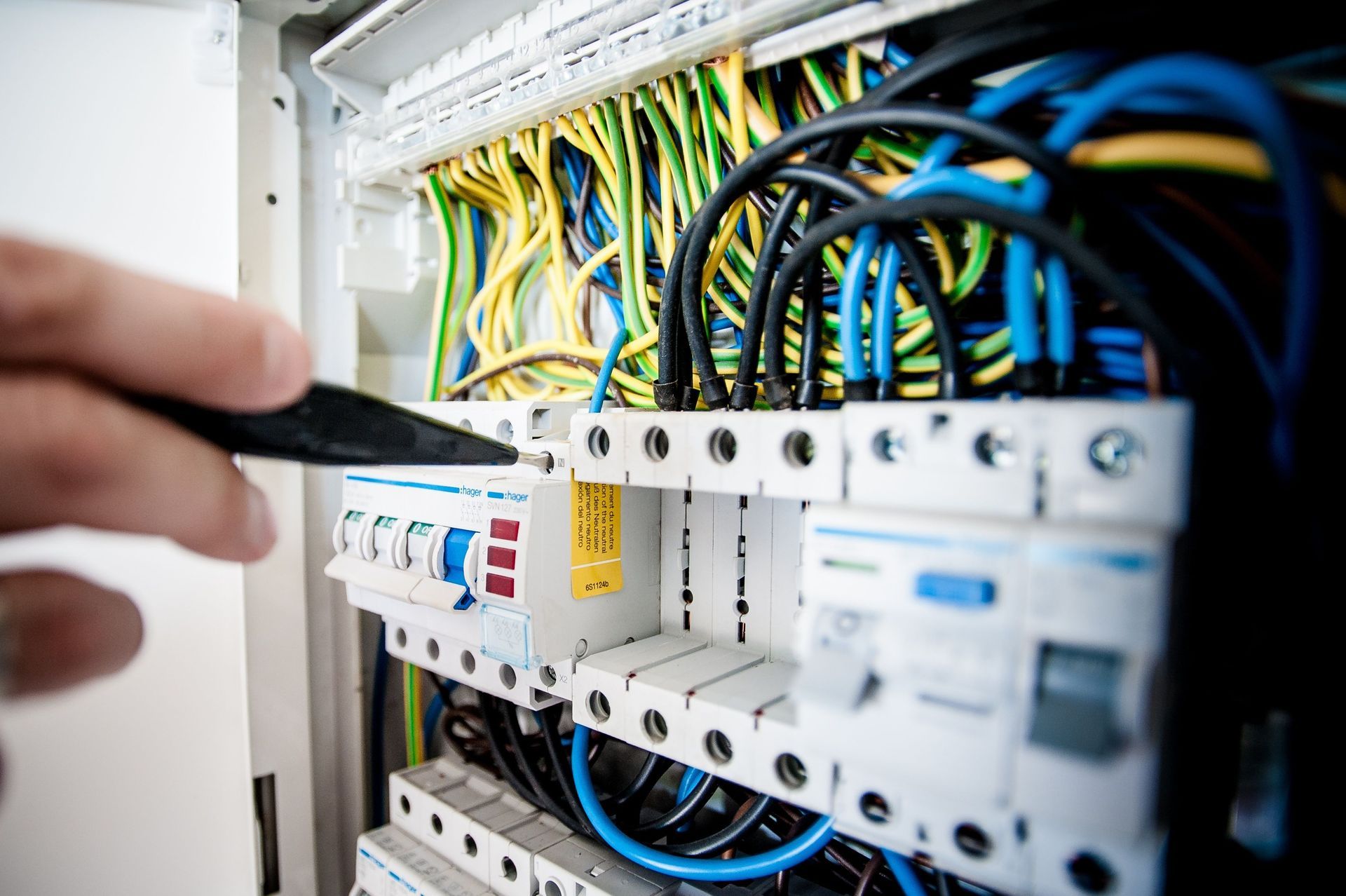 Technician testing wires in an electrical control panel with blue and yellow cables
