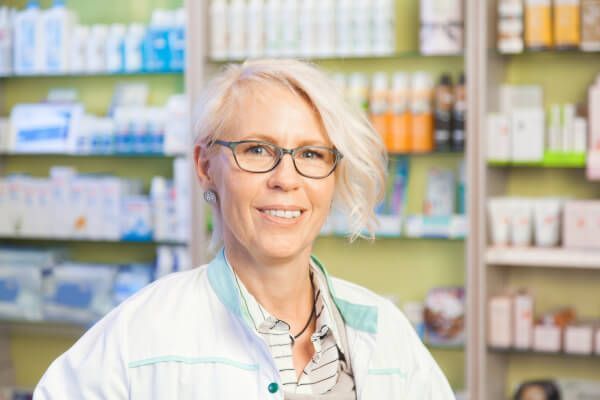 Eine Apothekerin mit Brille lächelt in einer Apotheke.