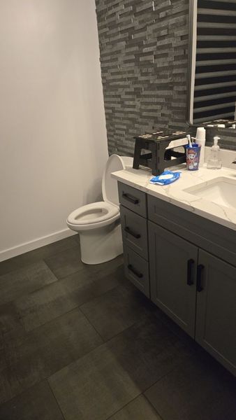 Small bathroom with dark tile floor, toilet, and gray vanity with sink and toiletries.
