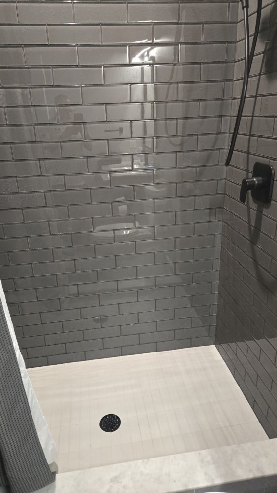 Gray-tiled shower stall with white floor and a small black drain.