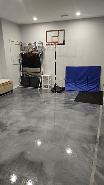 Empty garage with a basketball hoop, storage rack, folded chairs, and a blue mat on the wall.