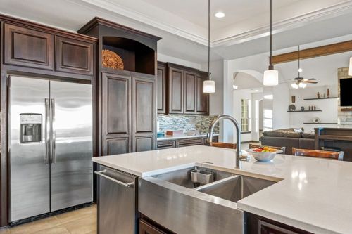 Modern kitchen with stainless steel appliances, dark wood cabinets, white island, and double sink