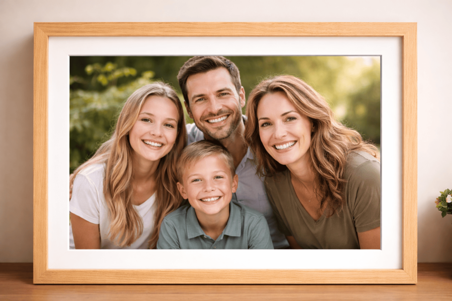 A framed family portrait featuring four smiling people outdoors, set against a blurred greenery background.