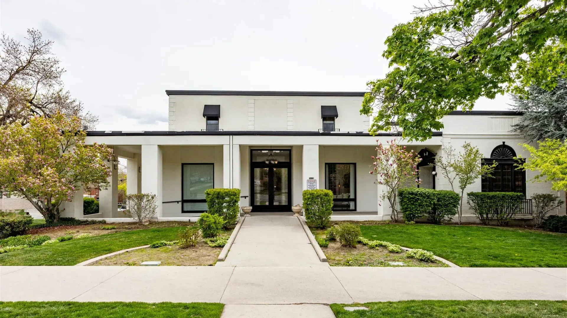 A white, single-story building with a front portico and a central walkway, set back from a sidewalk with grassy lawns.