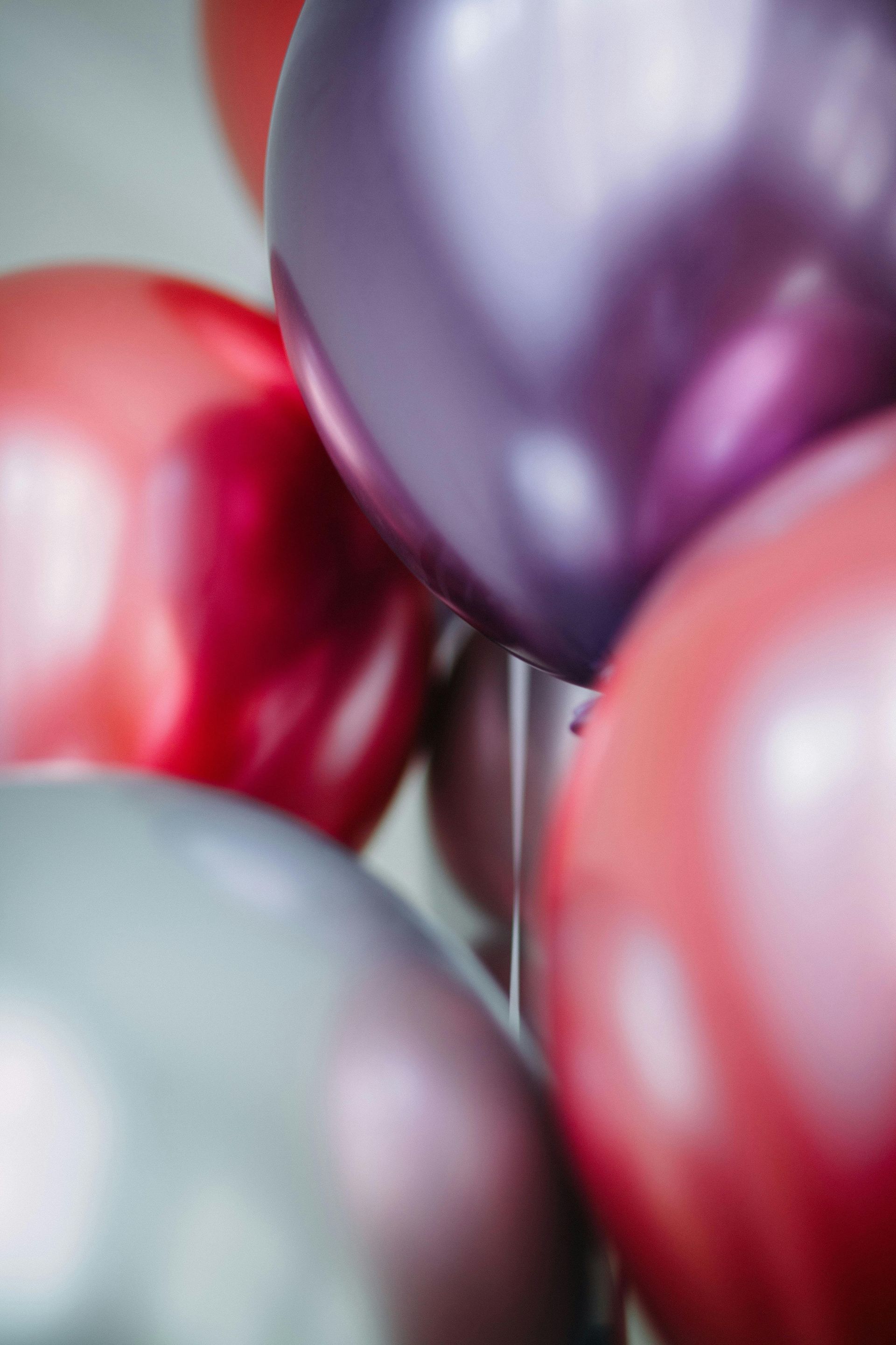 A close-up of shiny, metallic balloons in shades of red, purple, and silver clustered together.