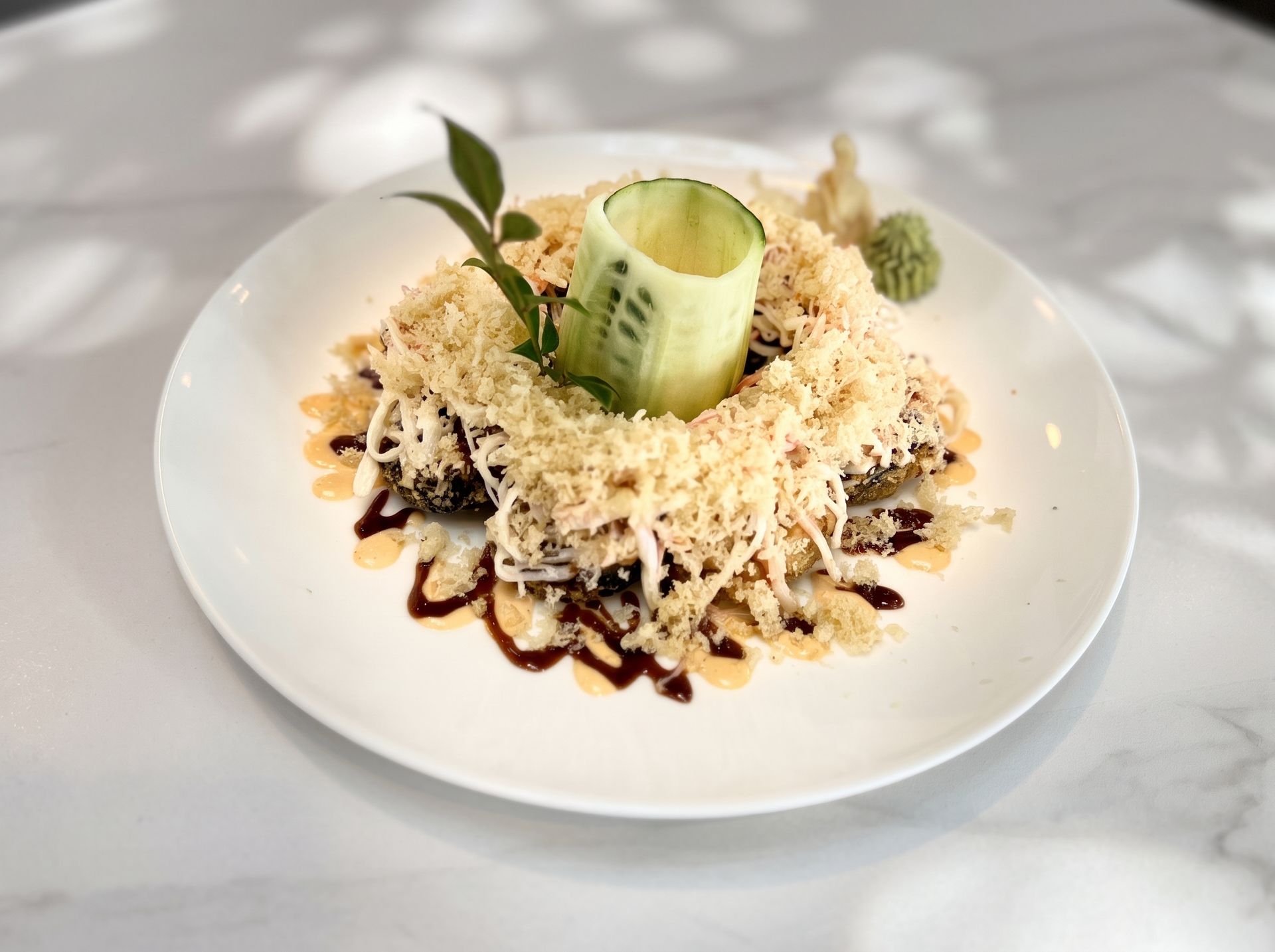 Plated dessert topped with shredded cheese and garnished with a cucumber roll and basil leaf