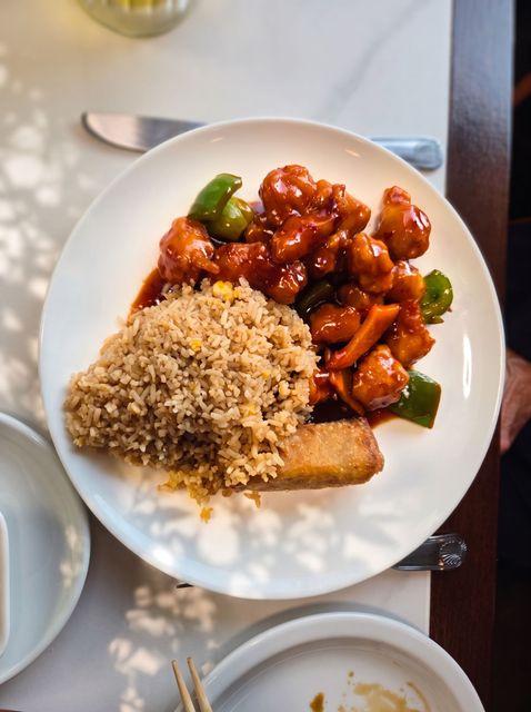 White plate with rice, saucy chicken, and vegetables on a café table