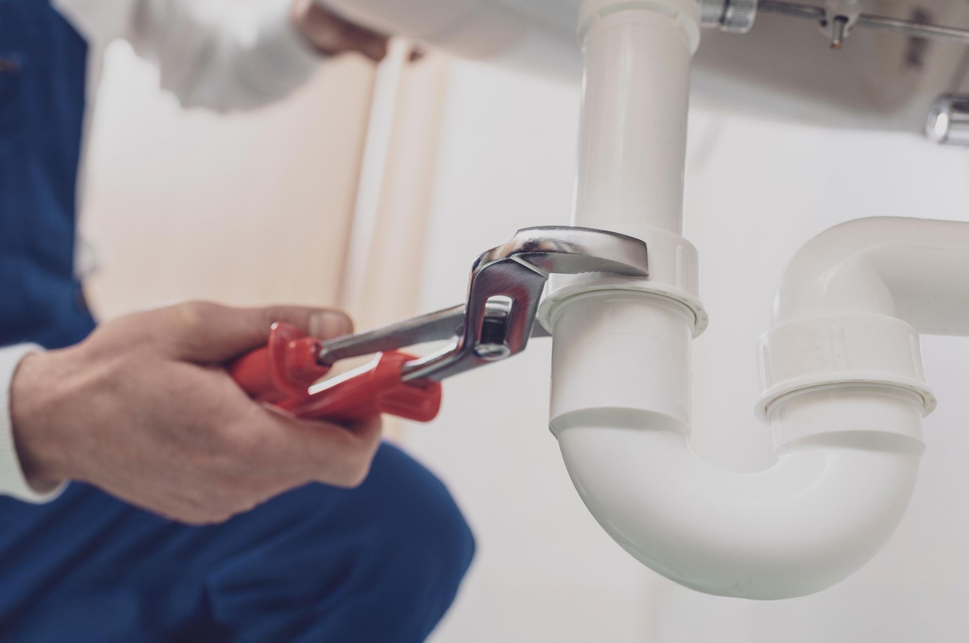 Plumber using a wrench on white pipes under a sink.