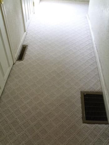 Hallway with light beige patterned carpet, two floor vents, and closed white doors.