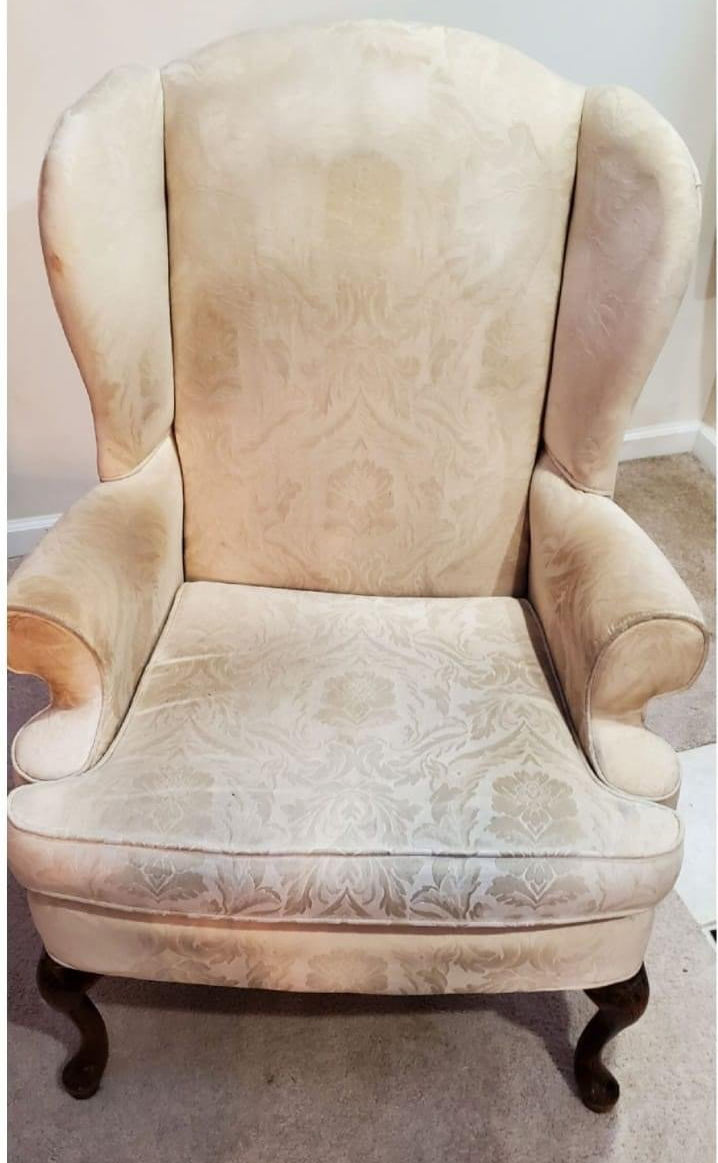 Cream-colored wingback chair with dark wooden legs, showing signs of wear and staining.