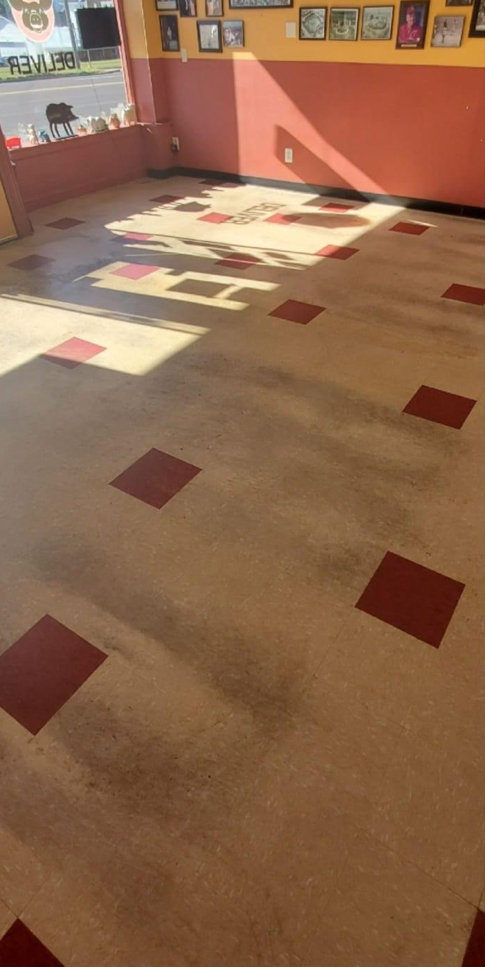 Interior of a building with a light beige floor with red square inlays. Sunlight streams in from a window on the left.
