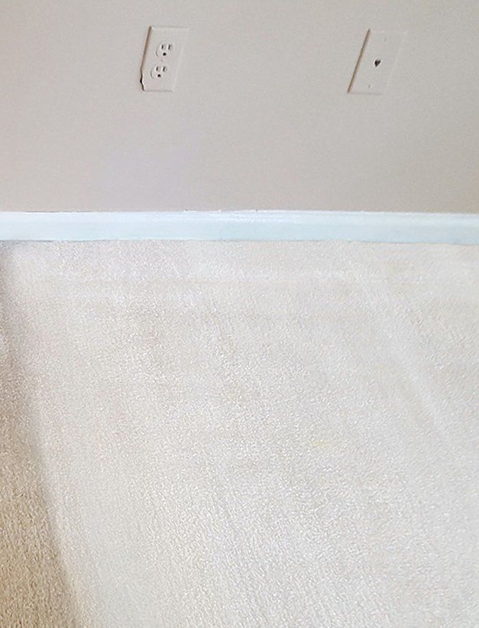 Off-white carpet against a wall with a light blue baseboard and two electrical outlets.