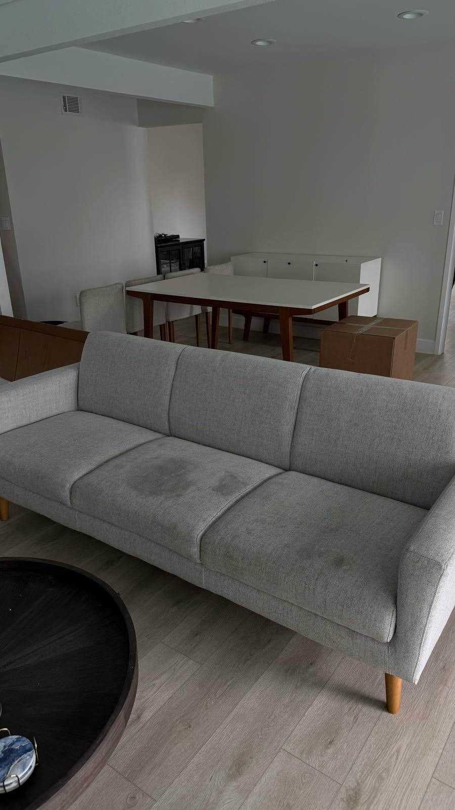 Gray sofa with stains in a living room; table and chairs in background.