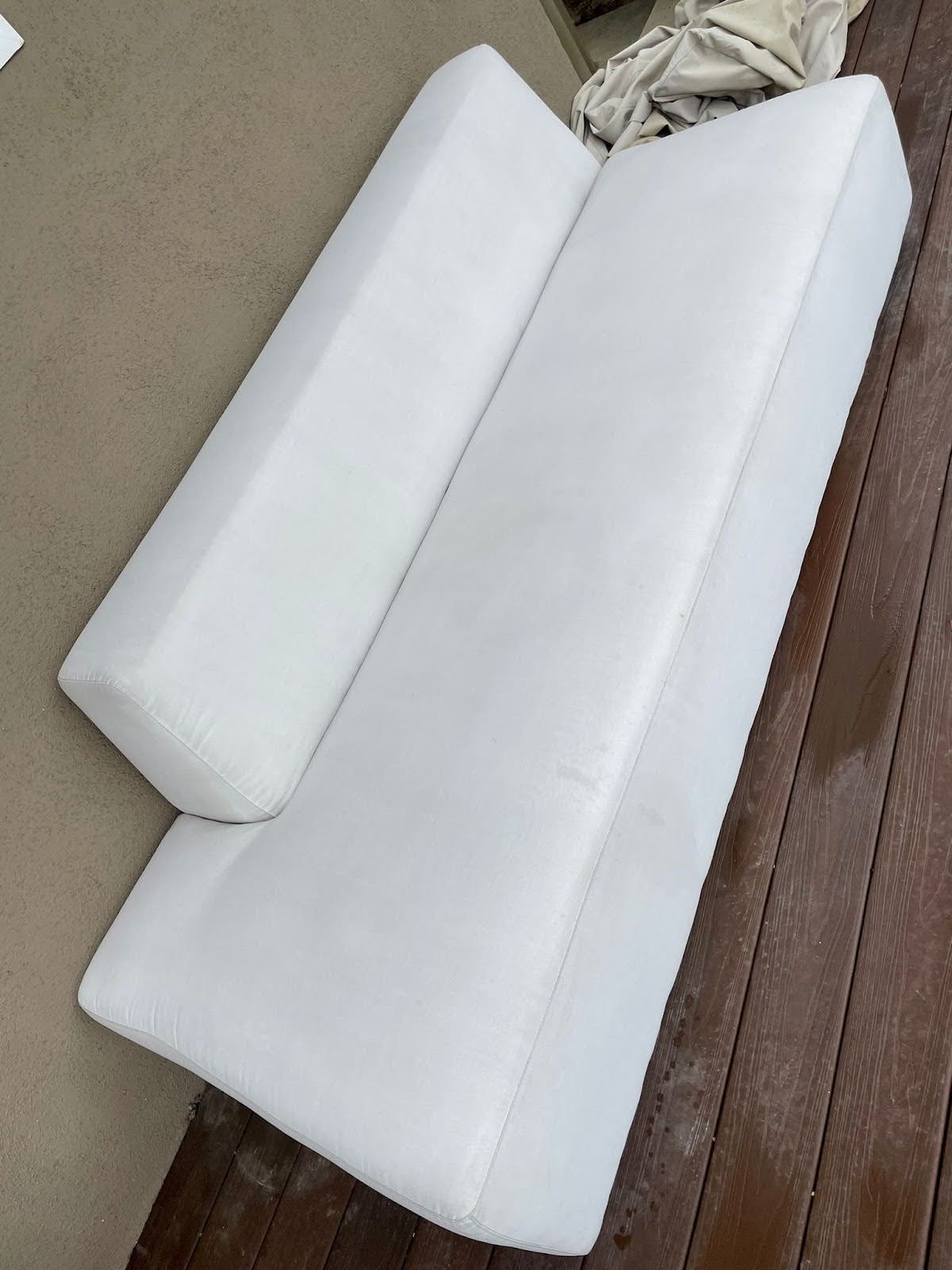 White rectangular cushions on a wooden deck. One smaller cushion angled against a larger one.