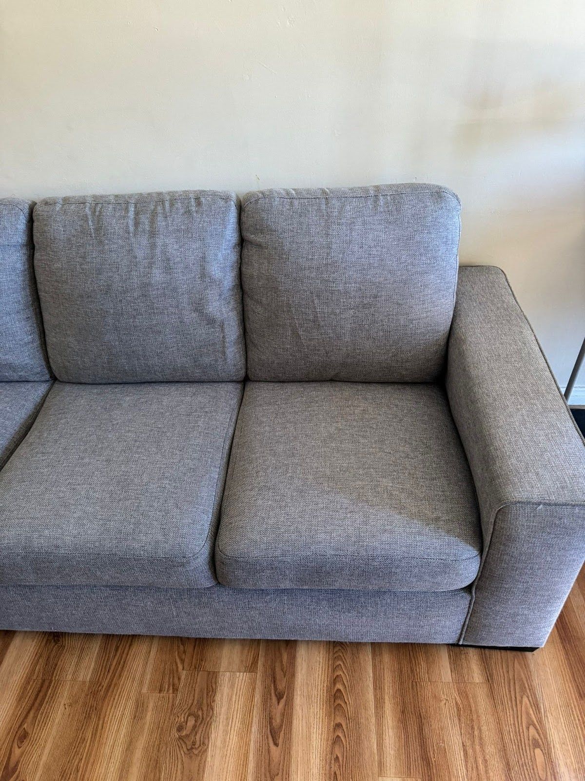 Gray upholstered sofa against a light wall, with wooden floor.