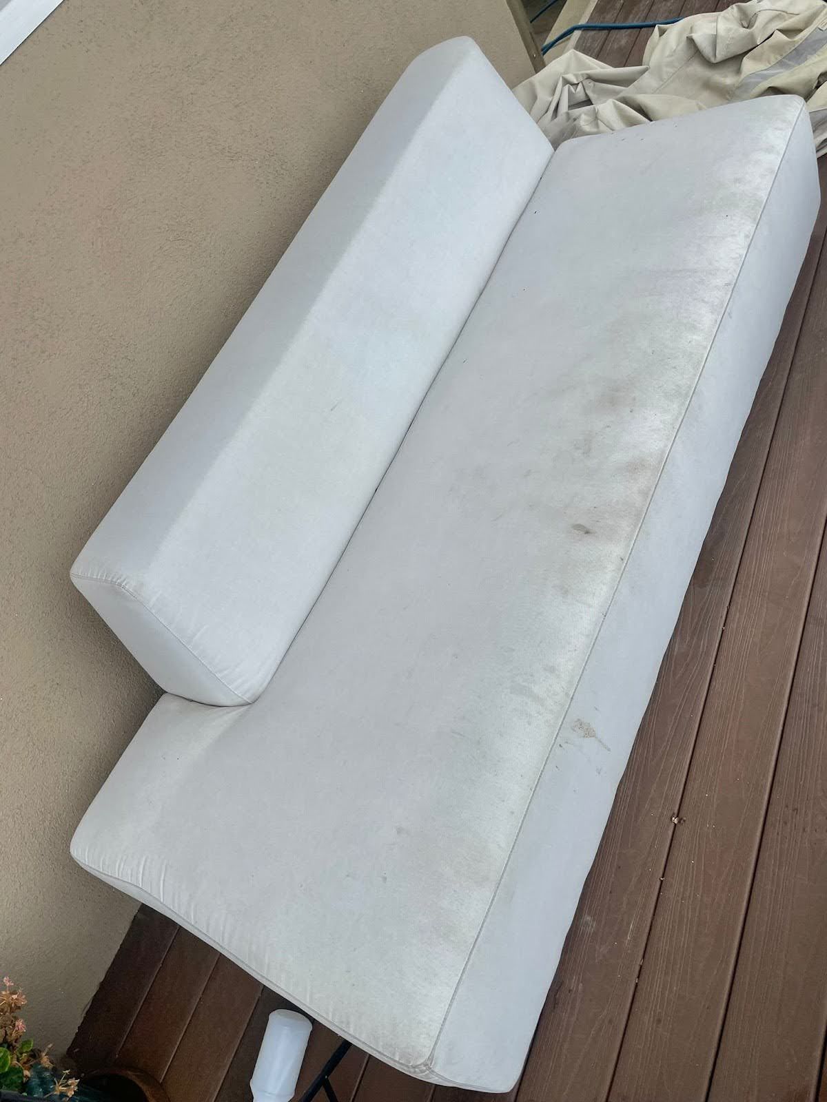White outdoor sofa cushions on a brown wooden deck, with a visible stain on one cushion.