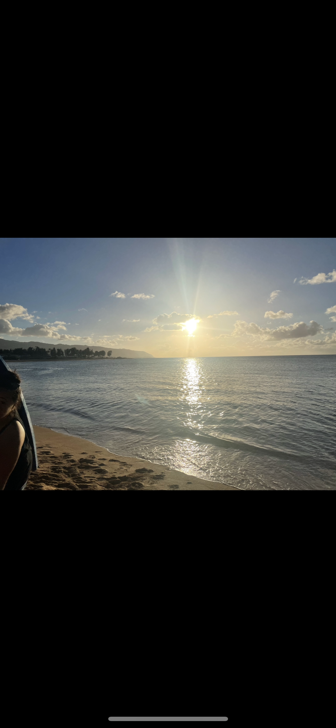 A person is standing on a beach watching the sun set over the ocean.