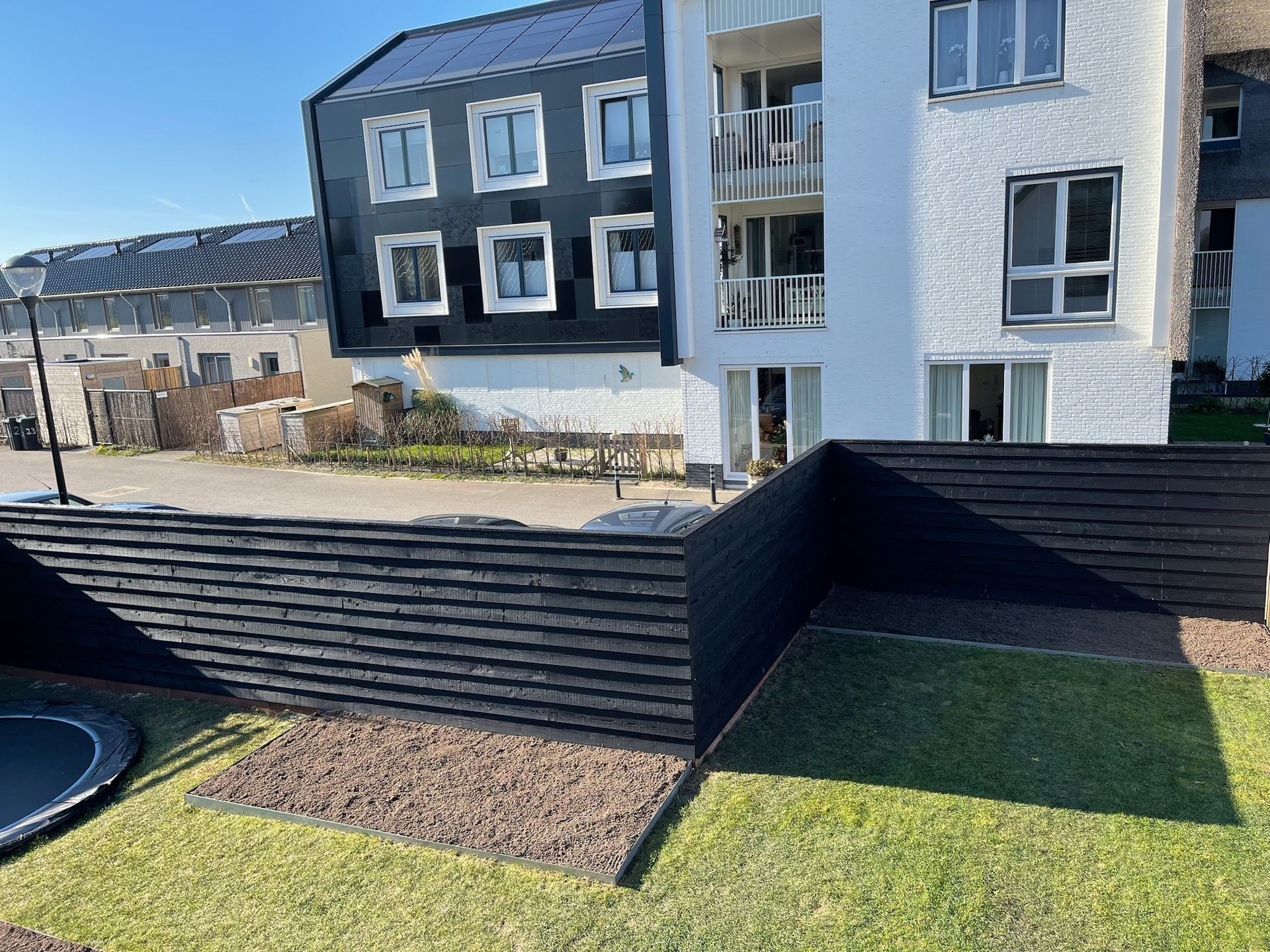 Een zwart lattenhek voor een modern gebouw met een zwart-witte gevel op een zonnige dag.