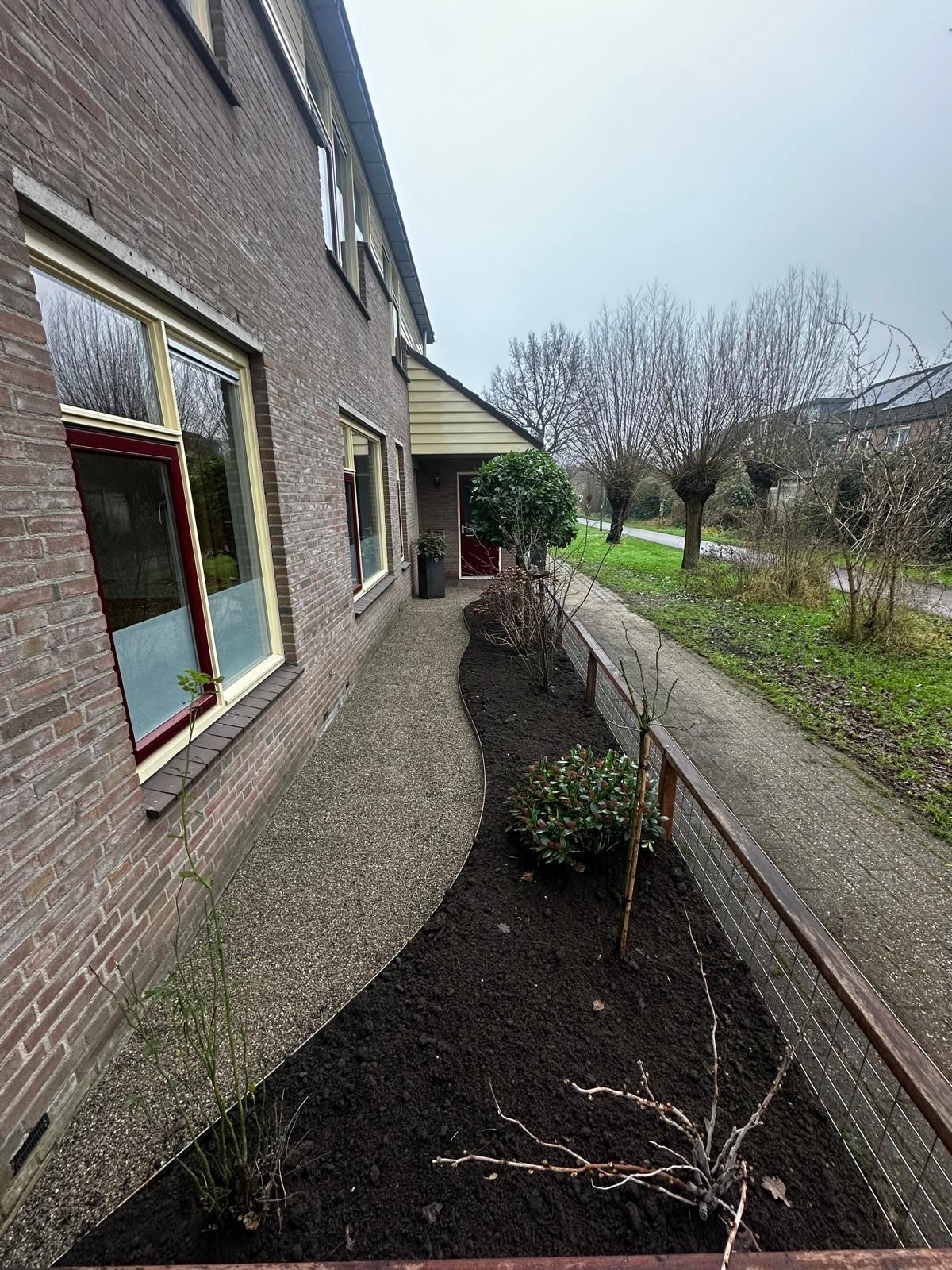 Bakstenen gebouw met pad, bloembed en wandelpad. Bewolkte dag.