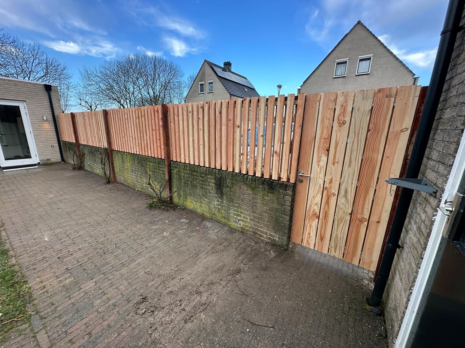 Houten schutting bovenop een betonnen muur in een achtertuin met bakstenen bestrating.
