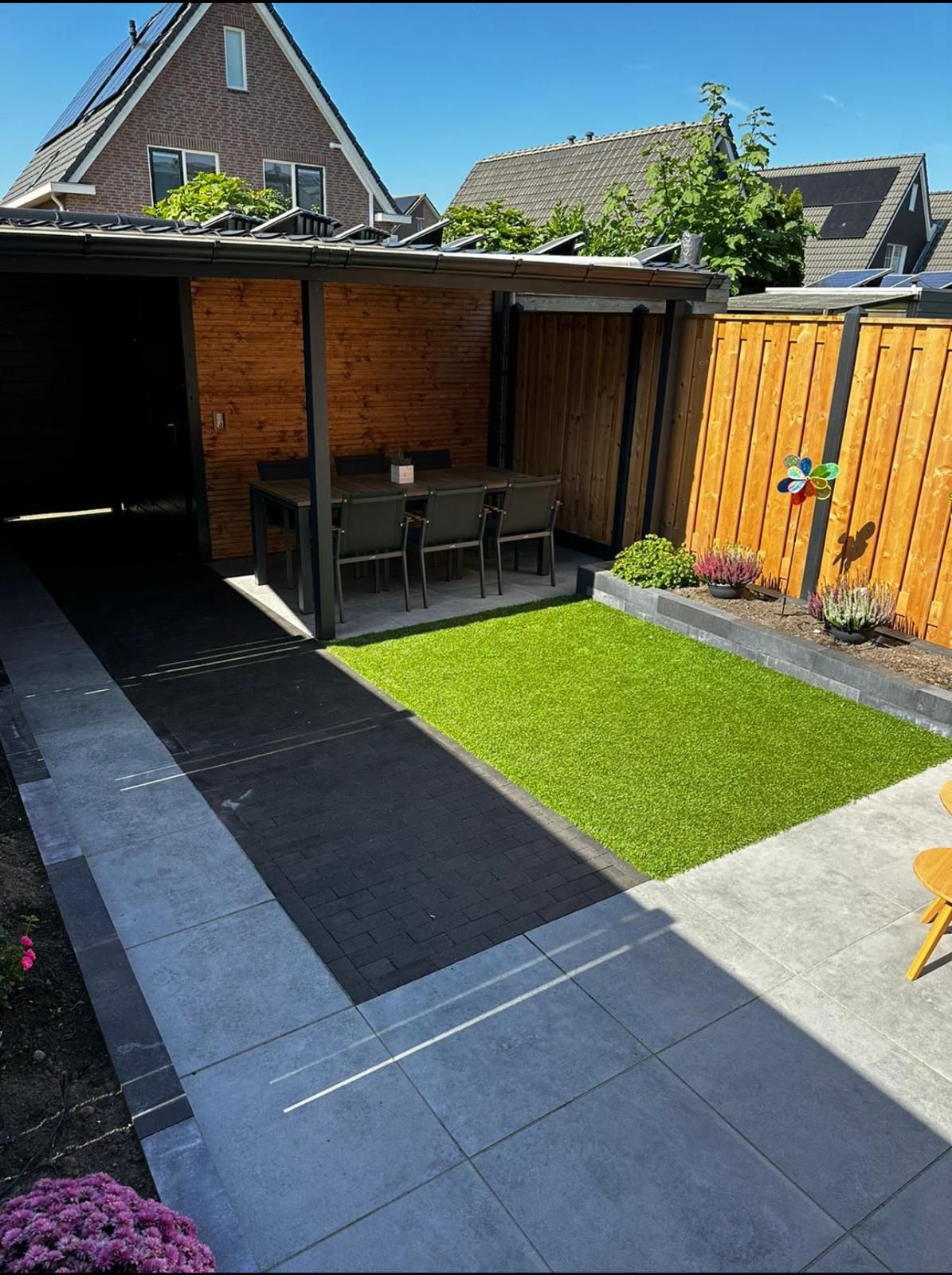 Terras in de achtertuin met eethoek, kunstgras en houten schutting.