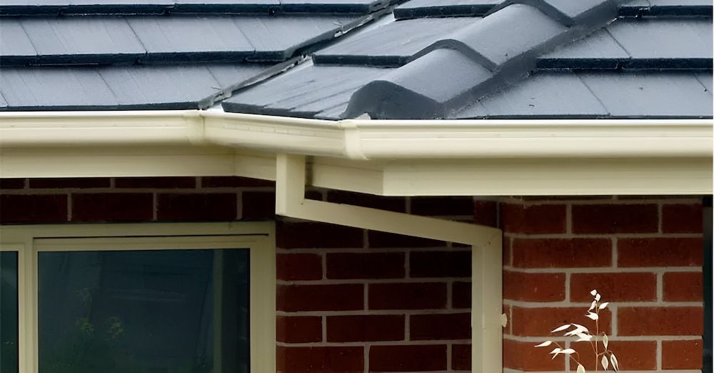 A Brick House With A White Gutter And A Black Tile Roof — The Gutter Guy NSW in Tarrawanna, NSW