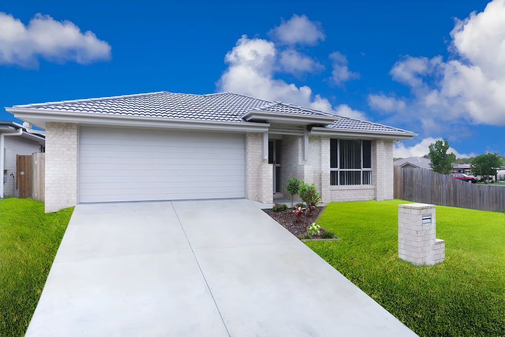 A White House With A Concrete Driveway And A White Garage Door — The Gutter Guy NSW in Shellharbour, NSW