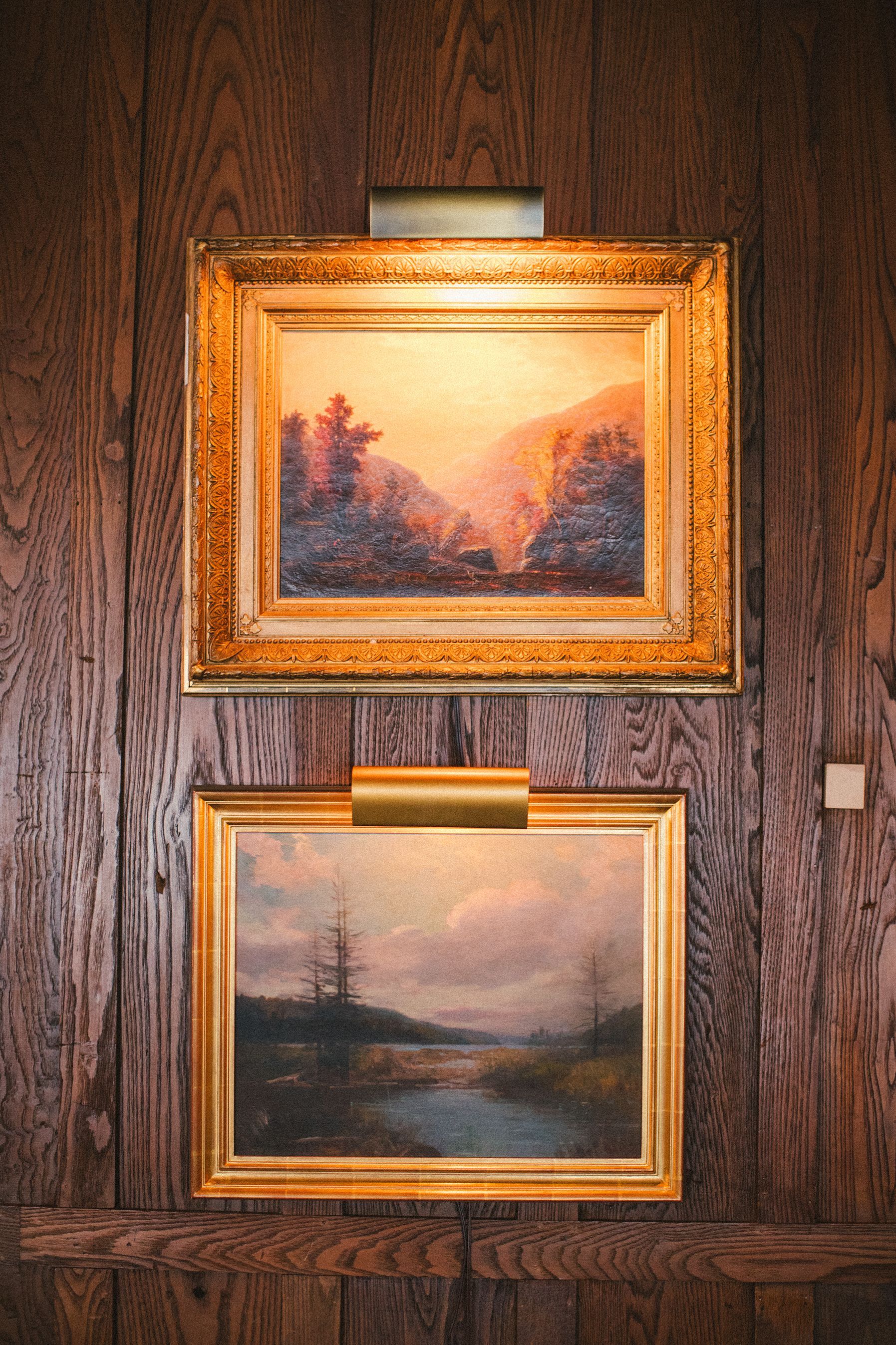 Two paintings are hanging on a wooden wall.