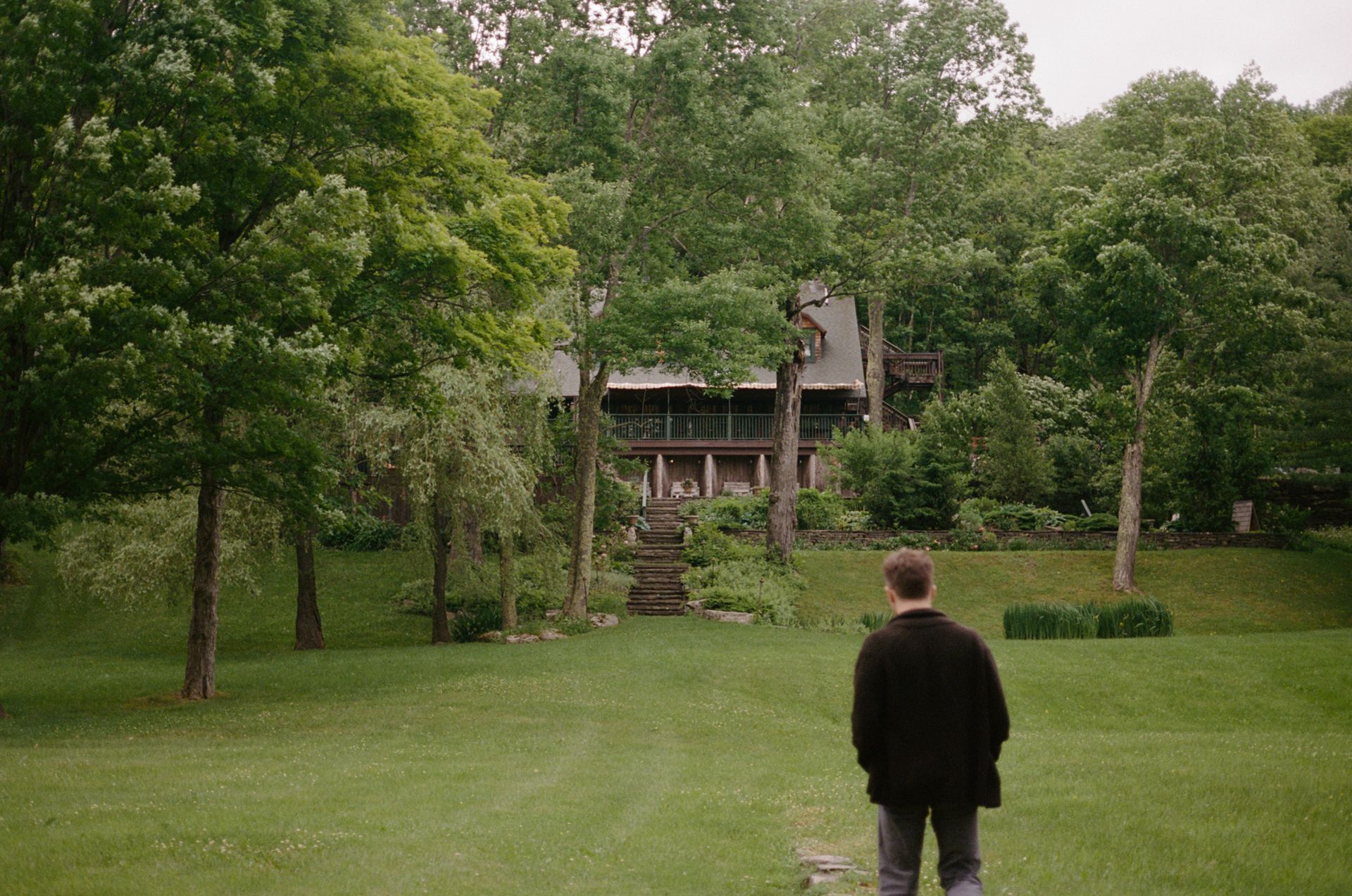 A man is standing in a grassy field in front of a house.