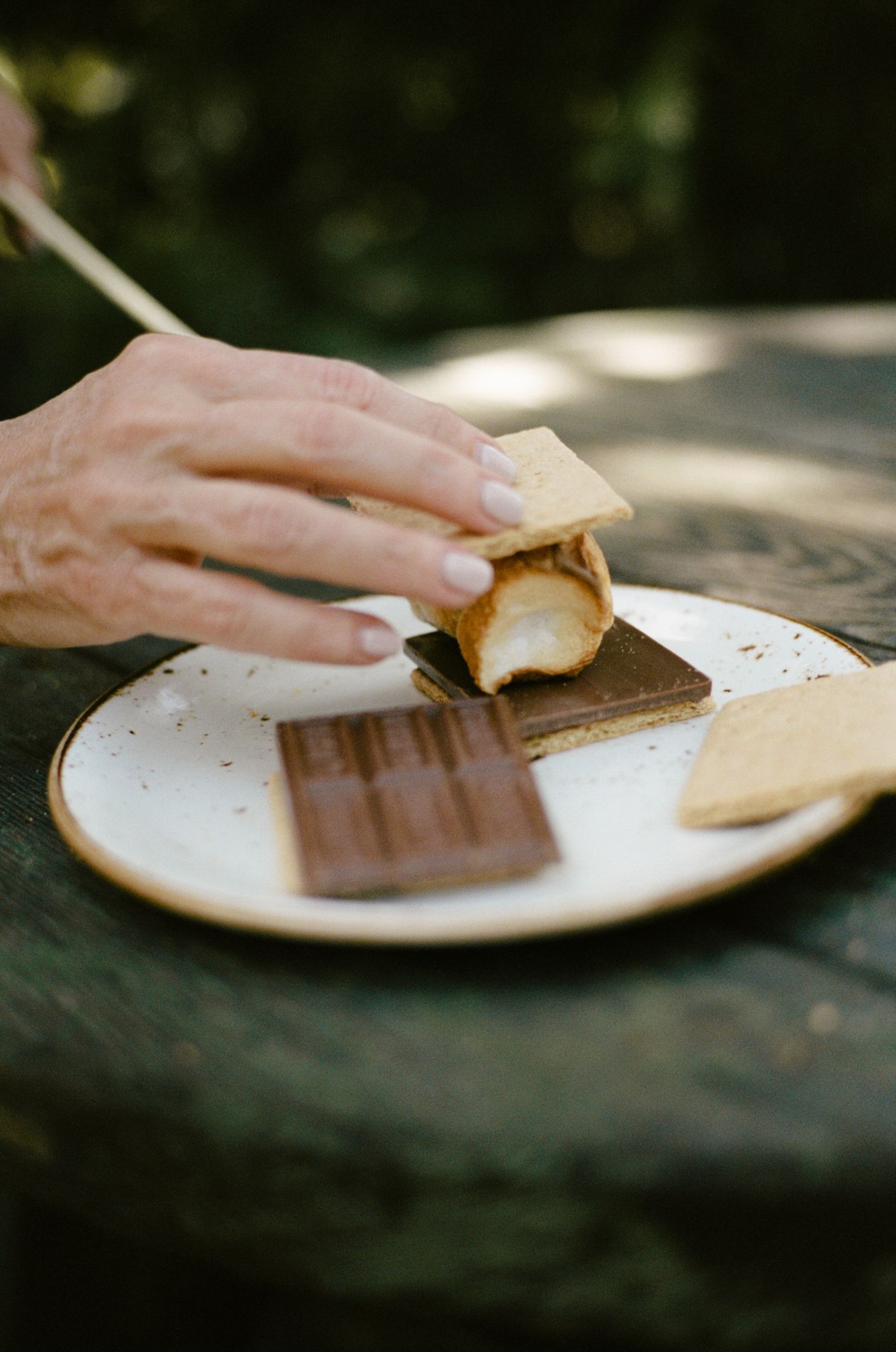 A person is eating a s'more on a plate with a fork.