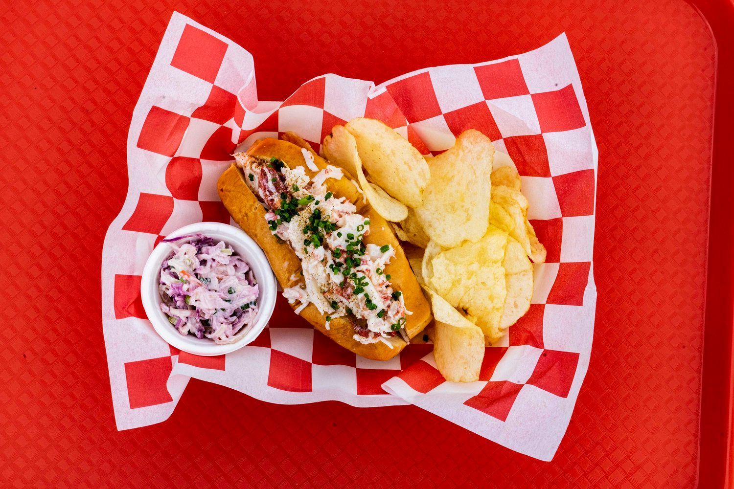A hot dog and chips are on a checkered paper on a red tray.