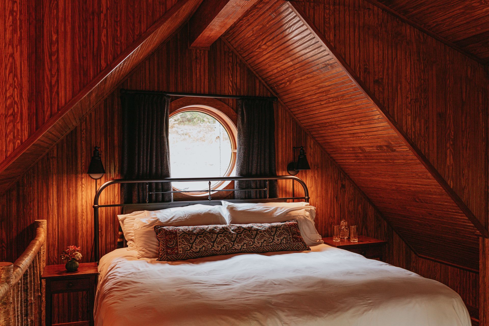 There is a bed in the attic with a round window.