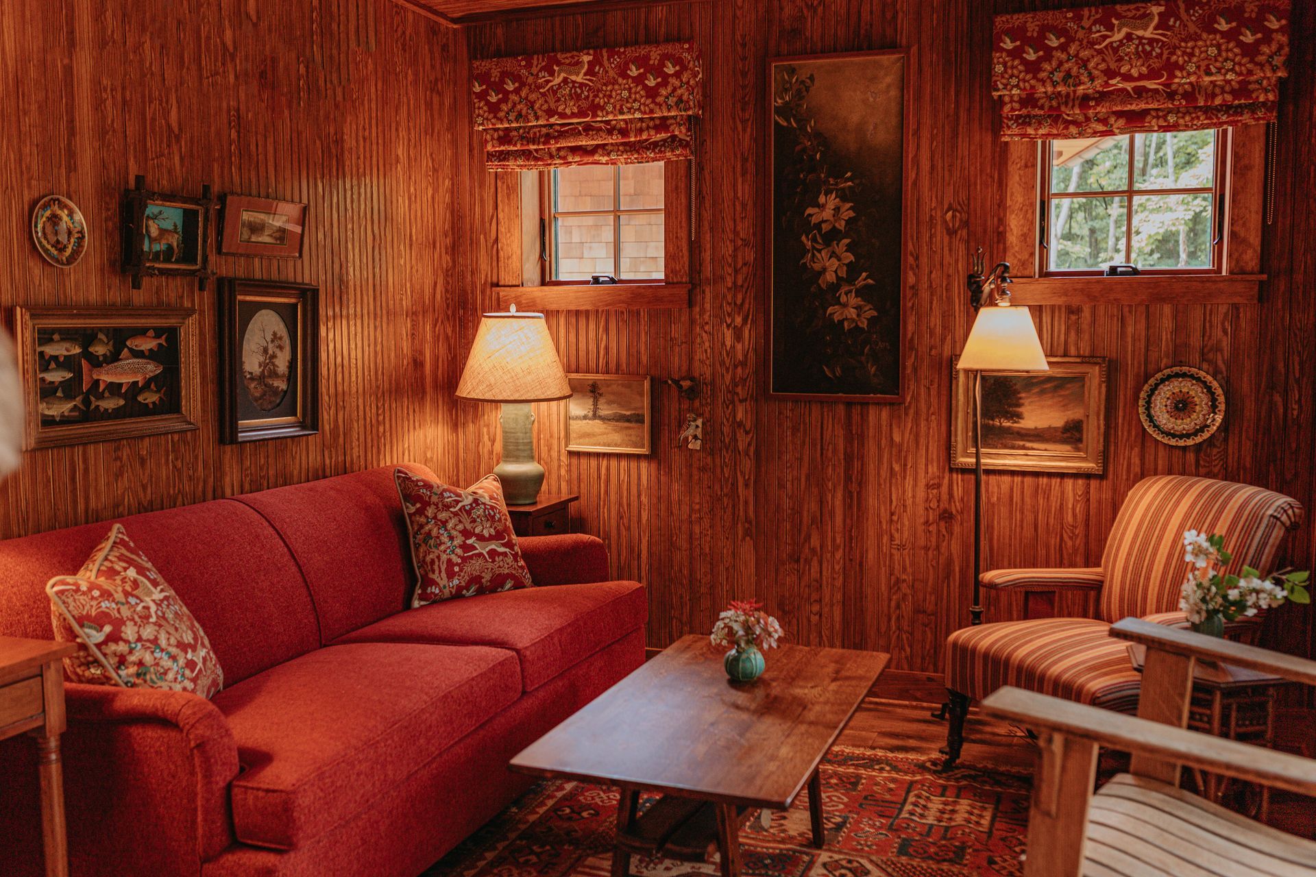 A living room with a red couch , chair , coffee table and lamps.