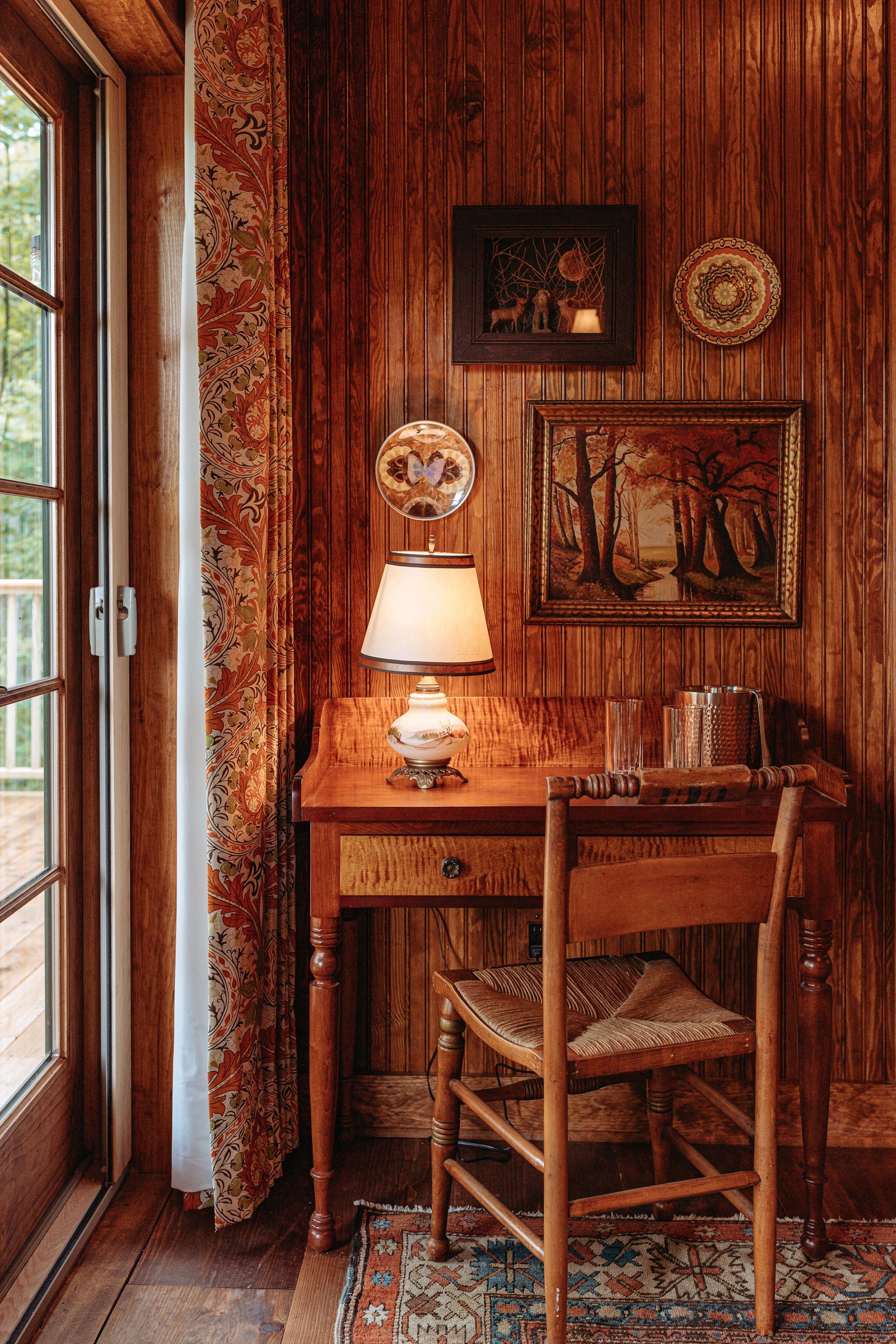 A wooden desk with a chair and a lamp in a room with wood paneling.