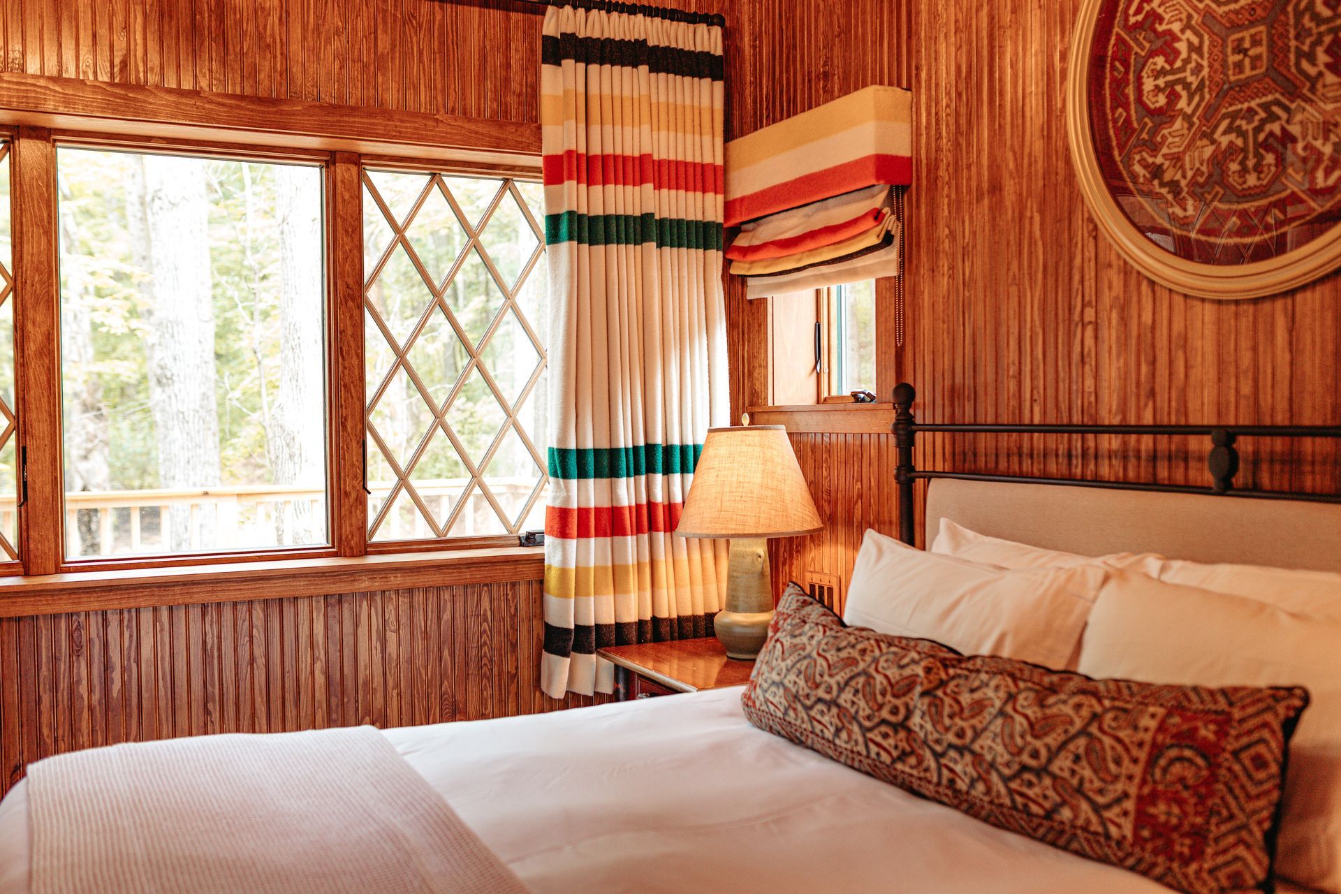 A bedroom with a bed , window , lamp and striped curtains.
