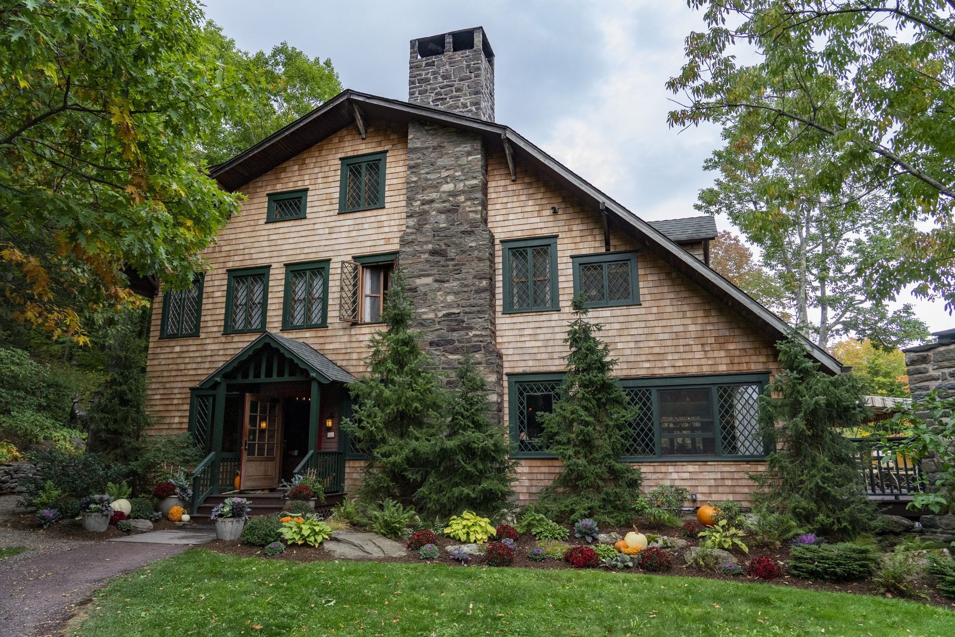 A large brick house with a stone chimney is surrounded by trees.