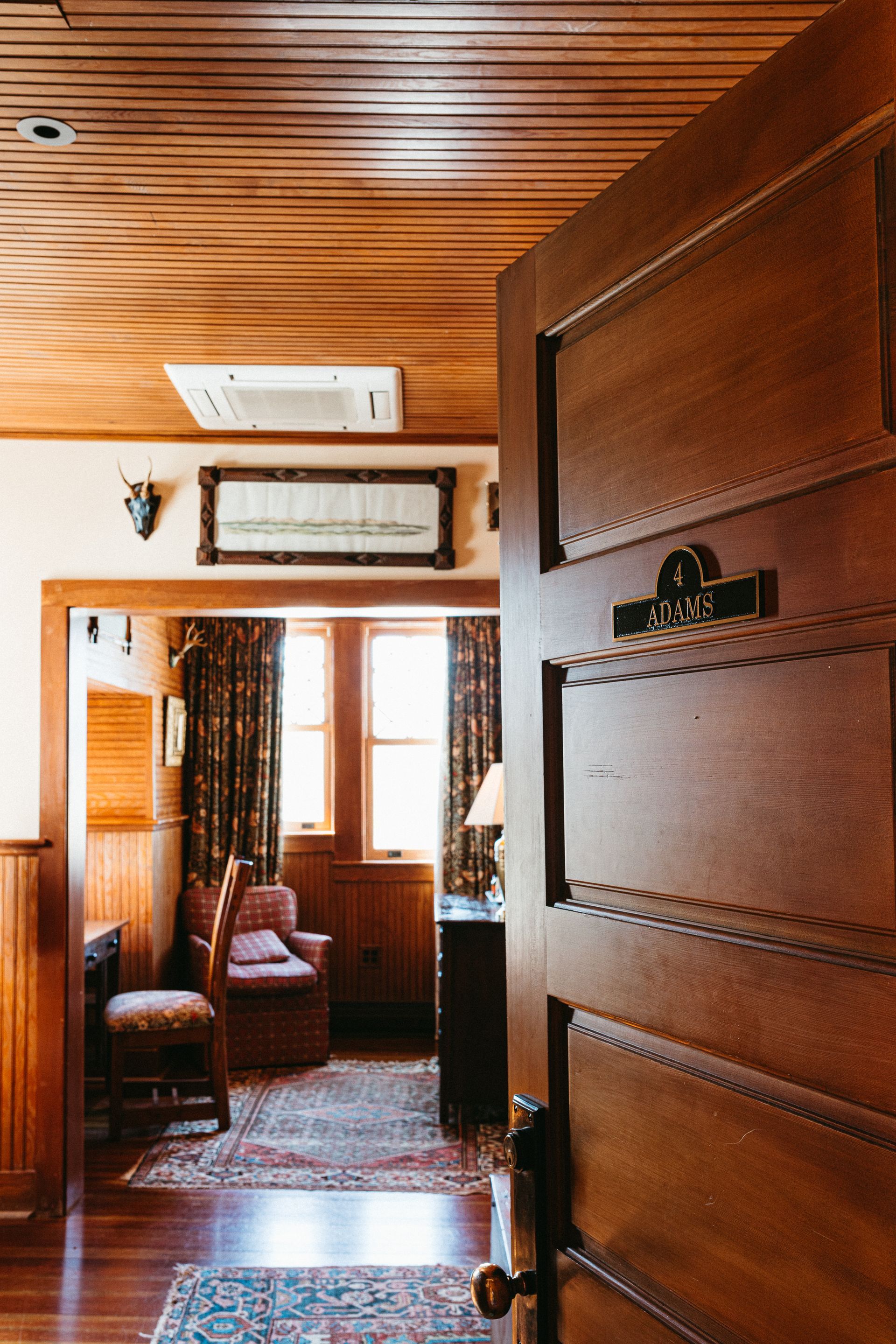 A wooden door is open to a living room with chairs and a rug.