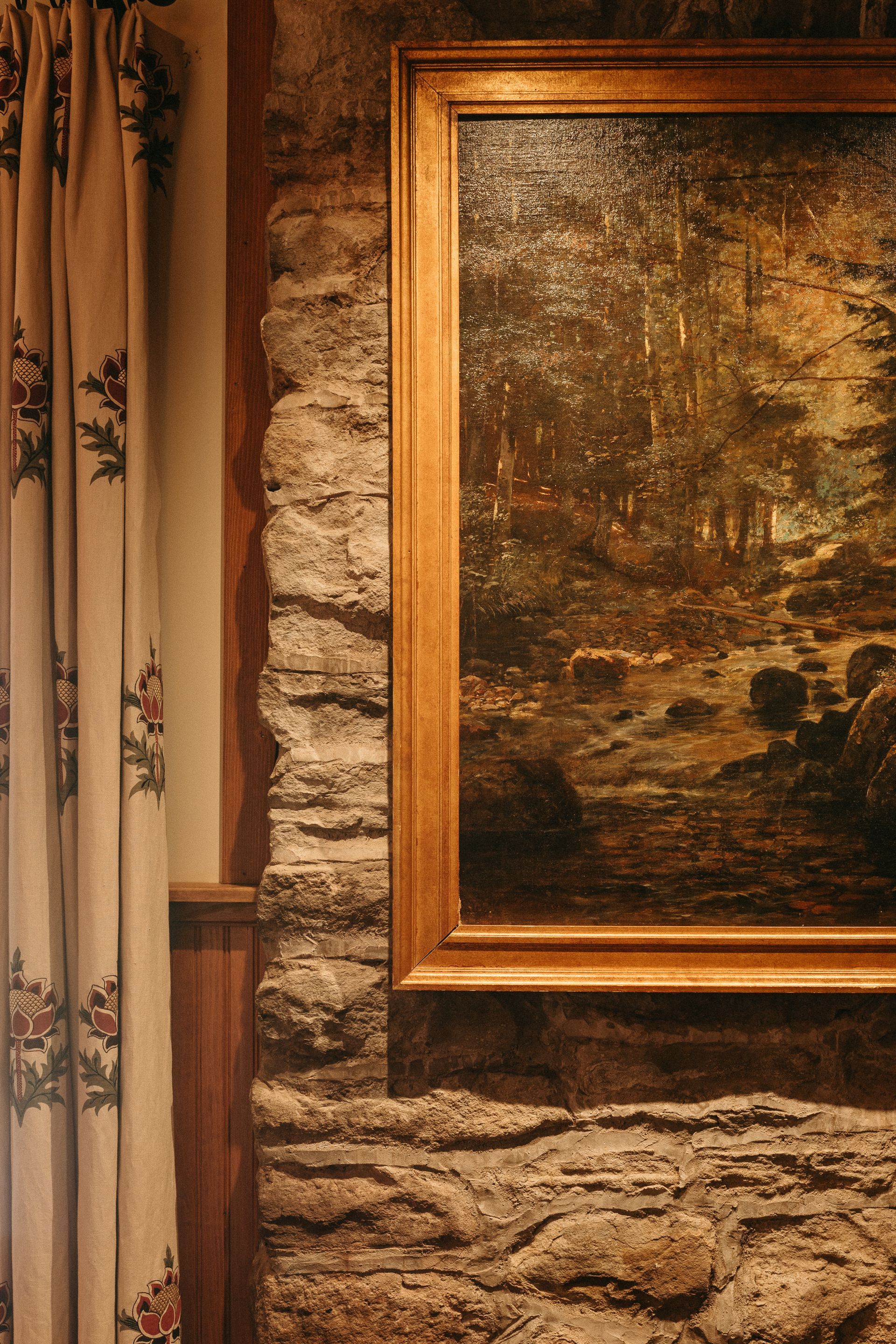 A painting is hanging on a stone wall next to a fireplace.
